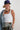 A  woman wearing a white ribbed tank top, a navy trucker hat with a colorful butterfly embroidered patch, a denim jacket draped over her shoulder, and camo pants-Bandana-Print-Large-Square-Scarf-Sage-Fleastyle