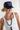 A woman wearing a navy blue trucker hat with a colorful embroidered butterfly on the front, paired with a white ribbed tank top and a long black beaded necklace-Butterfly Patch Trucker Hat - Navy-FleaStyle.