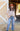A woman stands outdoors in front of a yellow barn wall, wearing a rust-colored flat-brim hat, a sheer blush flowy pleatd blouse, and floral embroidered blue jeans -Floral Embroidered High Waist Flare Jeans-FleaStyle