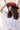 A woman with long, curly dark brown hair wearing a rust flat brim fedora style hat and an blush  ruffled blouse, outdoors against a yellow barn-Lenny_Wool_Short-Brim_Hat_-_Rust-FleaStyle