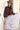 A woman wearing a brown ruffled blouse, a blush pleated tiered maxiskirt, a western belt with a heart-shaped buckle, and a beige cowboy hat, standing outdoors in front of a rustic barn-Pliss_Tiered_Maxi_Skirt-FleaStyle