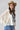 A woman wearing a camel cowboy hat,poncho-style top features an oversized batwing silhouette, vintage-inspired Free Bird graphic and sheer lace sleeves, and blue jeans, photographed against a light gray studio background.--Free_Bird_Lace_Graphic_Tee_Poncho_Top_-_Ivory-FleaStyle