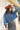 A woman wearing rust cowboy hat, a blue denim distressed raw hemmed cropped jacket, a sheer lace long sleeve top, and a long flare dark olive skirt with silver studs, standing outdoors in front of a yellow wooden barn door-Cropped_Distressed_Denim_Jacket-FleaStyle