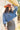 A woman wearing rust cowboy hat, a blue denim distressed raw hemmed cropped jacket, a sheer lace long sleeve top, and a long dark flare olive skirt with silver studs, standing outdoors in front of a yellow wooden barn door-Suede_Western_Studded_Maxi_Skirt_-_Olive-FleaStyle