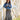 A woman wearing rust cowboy hat, a blue denim raw hemmed cropped jacket, a sheer lace long sleeve top, and a long flare dark olive skirt with silver studs, standing outdoors in front of a yellow wooden barn door-Suede_Western_Studded_Maxi_Skirt_-_Olive-FleaStyle