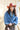 A woman wearing a distressed blue cropped denim jacket with raw frayed edges, a rust curled brim cowboy hat that's warm and spicy, and a brown studded skirt,  outdoors against a light-colored wooden barn-Rider Wool Cowboy Hat - Rust-FleaStyle