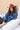 A woman wearing rust cowboy hat, a blue denim  distressed raw hemmed cropped jacket, a sheer lace long sleeve top, and a long flared dark olive skirt with silver studs, standing outdoors in front of a yellow wooden barn door-Cropped_Distressed_Denim_Jacket-FleaStyle