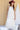 A woman wearing a maroon curl-brimmed cowboy hat and an ivory halter dress, posing in front of a light beige wooden barn wall-Rider_Wool_Cowboy_Hat_-_Maroon-FleaStyle.