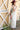 A woman wearing an ivory tiered maxi dress, a maroon curled brim cowboy hat, and a colorful patterned "Rodeo" scarf standing in front of a yellow barn door-Rodeo_Navy_and_Orange_Large_Square_Scarf-FleaStyle