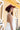 A woman wearing a maroon curl-brimmed cowboy hat and an ivory halter dress, posing in front of a light beige wooden barn wall-Rider_Wool_Cowboy_Hat_-_Maroon-FleaStyle.