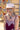 A woman wearing a  blush flat brim hat with a feather accent, a chunky stone necklace, and a burgundy lace-trim dress, posed outdoors against a colorful floral wall and barn-Stevie Wool Wide-Brim Hat - Blush