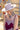 A woman wearing a  blush flat brim hat with a feather accent, a chunky stone necklace, and a burgundy lace-trim dress, posed outdoors against a colorful floral wall and barn-Stevie Wool Wide-Brim Hat - Blush