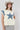 A woman wearing a cream-colored sleeveless top with a large blue star patch and  blue patterned lace appliques on the shoulders, paired with a beige cowboy hat and a Denim_Star_Patchwork_Sleeveless_T-Shirt-FleaStyle