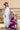 A woman wearing a burgundy maxi dress with light pink lace trim and a ivory wide-brim hat, standing outdoors in front of a yellow barn-Lace Trim Maxi Dress - Blush/Maroon