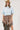 A woman wearing a light blue cropped knit sweater and a brown plaid high-low skirt with frayed edges, wearing a tan cowboy hat --Plaid_Asymmetrical_Tiered_Midi_Skirt-FleaStyle