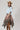 A woman wearing a light blue cropped knit sweater and a brown plaid high-low skirt with frayed edges, wearing a tan cowboy hat --Plaid_Asymmetrical_Tiered_Midi_Skirt-FleaStyle