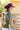 A woman wearing a western-style olive faux leather jacket covered in cream appliqué, silver-tone studs and turquoise-inspired details paired with  a maroon cowboy hat, and brown boots and lace tired dress-Turquoise Studded Leather Jacket - Olive-FleaStyle-