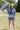 Woman holding a soccer ball wearing a cap with a 'Futbol Y'all' design and a Denim-Star-Graphic-T-Shirt-Dusty-Blue-Fleastyleon a grassy field .
