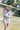 Woman in a Short-Sleeve-Striped-Romper-Blue-Fleastyle, blue bandana and cowboy hat walking on a soccer field.
