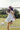 Woman in a -Toile-Print-Babydoll-Dress-Blue-Fleastyle and brown straw cowboy hat standing next to a soccer ball on a grass field with a goal net in the background.