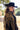 A woman wearing a black wool cowboy hat and a black fringed cape with ornate gold beaded embroidery, photographed outdoors in a sunlit field with trees and a barn-Rider Wool Cowboy Hat Black - Flea Style