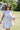 Woman in a -Toile-Print-Babydoll-Dress-Blue-Fleastyle and brown straw cowboy hat standing next to a soccer ball on a grass field with a goal net in the background.