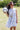 Woman in a -Toile-Print-Babydoll-Dress-Blue-Fleastyle and brown straw cowboy hat standing next to a soccer ball on a grass field with a goal net in the background.