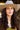 A smiling woman wearing a wide-brimmed light beige hat, a brown dress with olive green lace trim, and a chunky gold necklace, posed against ayellow bar-Jenner Cowboy Cashmere Wool Hat - Stone