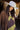 A woman wearing a sleeveless brown maxi dress featuring contrast olive lace detailing throughout for a rich, vintage-inspired feel paired with and a stone/beige cowboy hat, standing outdoors in front of a barn-Lace_Trim_Maxi_Dress_-_Brown_Chartreuse-FleaStyle