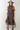 A woman wearing a brown leopard-print midi dress with sheer short sleeves and a high neck, styled with a flat-brimmed brown hat, a long gold-tone necklace, and brown boots against a light gray studio background-Animal_Print_Sheer_Overlay_Dress-FleaStyle.