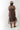 A woman wearing a brown leopard-print midi dress with sheer short sleeves and a high neck, styled with a flat-brimmed brown hat, a long gold-tone necklace, and brown boots against a light gray studio background-Animal_Print_Sheer_Overlay_Dress-FleaStyle.