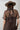 A woman wearing a brown leopard-print midi dress with sheer short sleeves and a high neck, styled with a flat-brimmed brown hat, a long gold-tone necklace, and brown boots against a light gray studio background-Animal_Print_Sheer_Overlay_Dress-FleaStyle.