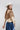 A woman wearing an ivory wide-flat brim hat, a beige suede- like fringed shrug, beige button up shirt and a blue denim skirt against a light gray studio background.-Suede_Fringe_Shrug_-_Tan-FleaStyle