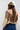 A woman shown from the back wearing an ivory wide-flat brim hat, a beige suede- like fringed shrug, beige button up shirt, blue denim skirt and cowboy boots against a light gray studio background.-Suede_Fringe_Shrug_-_Tan-FleaStyle