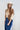 A woman wearing a tan button-up blouse with pearl embellished details, a maroon cowboy hat, and a dark blue denim midi skirt, photographed against a light gray studio background-Pearl_Embellished_Button_Down_Blouse_-_Tan-FleaStyle