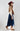 A woman wearing an ivory wide-flat brim hat, a beige suede- like fringed shrug, beige button up shirt and a blue denim skirt against a light gray studio background.-Suede_Fringe_Shrug_-_Tan-FleaStyle