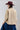 A woman wearing a tan button-up blouse with pearl embellished details, a maroon cowboy hat, and a dark blue denim midi skirt, photographed against a light gray studio background-Pearl_Embellished_Button_Down_Blouse_-_Tan-FleaStyle