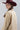A woman wearing a tan button-up blouse with pearl embellished details, a maroon cowboy hat, and a dark blue denim midi skirt, photographed against a light gray studio background-Pearl_Embellished_Button_Down_Blouse_-_Tan-FleaStyle