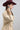 A woman wearing a tan button-up blouse with pearl embellished details, a maroon cowboy hat, and a dark blue denim midi skirt, photographed against a light gray studio background-Pearl_Embellished_Button_Down_Blouse_-_Tan-FleaStyle