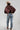 A woman wearing a brown satin cape-style blouse with a large bow at the neckline, a beige cowboy hat, and blue jeans, photographed against a plain light gray studio background-Exaggerated_Bow_Blouse_-_Rust-FleaStyle