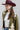 A woman wearing a maroon cowboy hat, olive green western-style jacket with cream and turquoise accents, a white ribbed crop top, blue jeans, and a pair of oval silver-toned concho style earrings with turquoise-colored inlay stones-Western_Inspired_Scalloped_Earrings-FleaStyle.