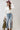 A woman wearing a white off-the-shoulder long-sleeve crop top, embroidered floral blue jeans and a  maroon cowboy hat, and holding an olive green faux leather jacket, against a light gray studio background-Floral_Embroidered_High_Waist_Flare_Jeans-FleaStyle.
