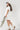 Woman wearing an ivory Floral-Embroidery-Cut-Out-Mini-Dress, cowboy boots, and a white cap with 'Texas' text on a white background-Fleastyle