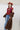 A woman wearing a maroon short-sleeve crewneck sweater with a red, orange, and white tiger print, paired with blue jeans, turquoise elongated concho earrings a long gold  necklace, a long brown faux fur coat and a rust cowboy hat-Tiger_Tapestry_Short-Sleeve_Sweater-FleaStyle