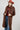 A woman wearing a long,  brown faux fur coat with a horse motif lining, paired with a rust-colored cowboy hat, a maroon tigher patterned top, and blue jeans against a gray background-Longline_Faux_Fur_Jacket_-_Brown-FleaStyle