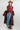 A woman wearing a maroon short-sleeve crewneck sweater with a red, orange, and white tiger print, paired with blue jeans, turquoise elongated concho earrings a long gold  necklace, a long brown faux fur coat and a rust cowboy hat-Tiger_Tapestry_Short-Sleeve_Sweater-FleaStyle
