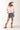 Woman wearing a pink shirt, High Rise Frayed Hem A Line Denim Shorts, and cowboy boots on a white background