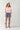 Woman wearing a pink shirt, High Rise Frayed Hem A Line Denim Shorts, and cowboy boots on a white background