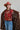A woman wearing a long,  brown faux fur coat with a horse motif lining, paired with a rust-colored cowboy hat, a maroon tigher patterned top, and blue jeans against a gray background-Longline_Faux_Fur_Jacket_-_Brown-FleaStyle