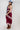 A woman wearing a  maxi dress in deep burgundy with light pink floral lace trim, styled with a dusty blue cowboy hat and holding a blue denim jacket against a plain white studio background.-Lace_Trim_Maxi_Dress_-_Blush_Maroon-FleaStyle
